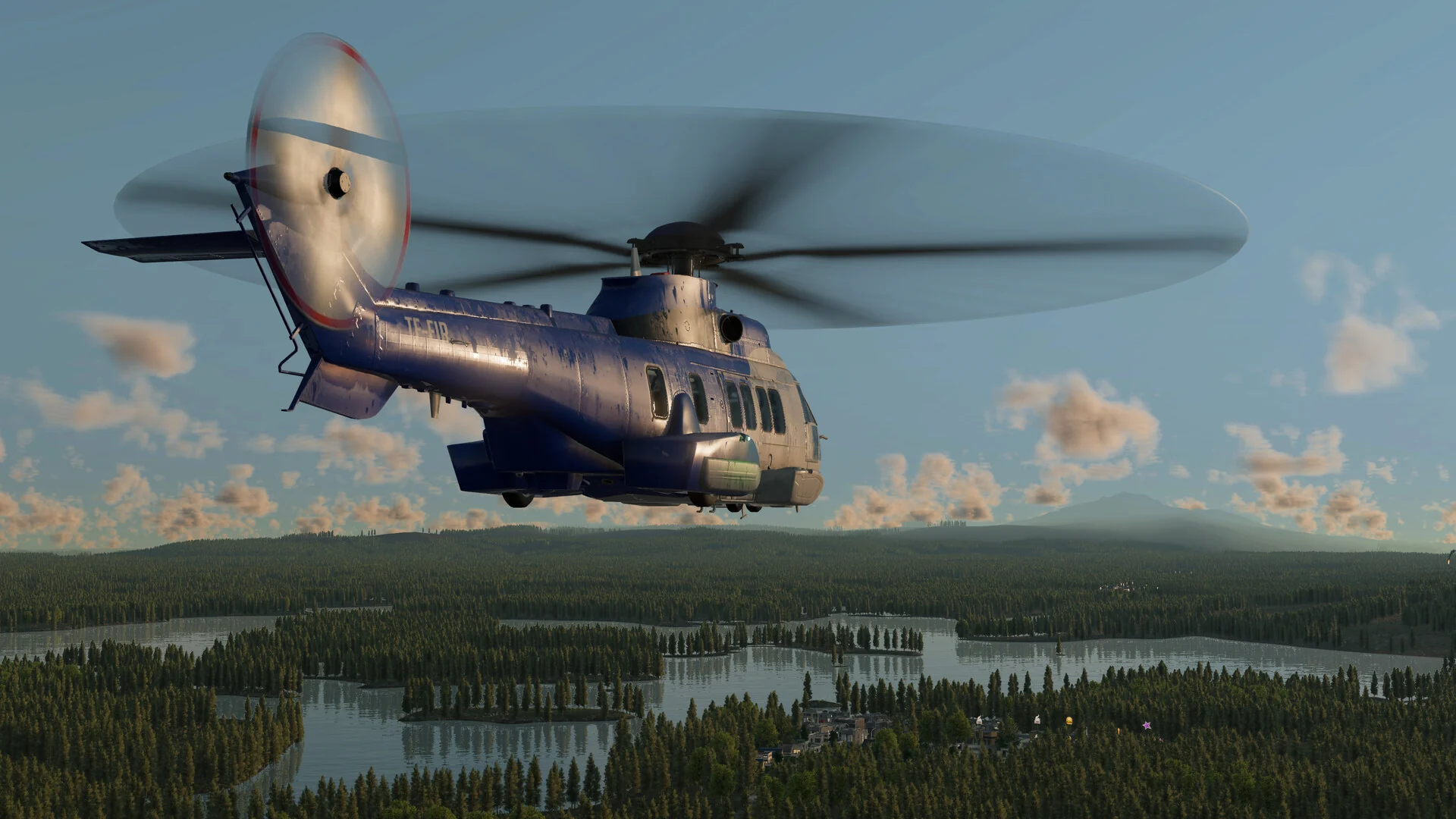 Large blue transport helicopter flying above lakes and a forested landscape